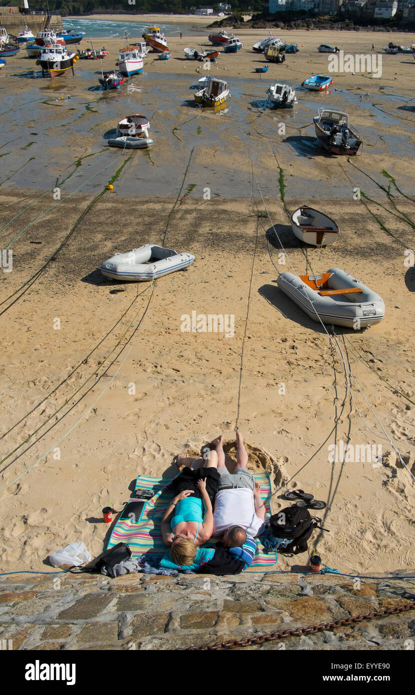 Man and woman sunbathing on harbour beach at St Ives, Cornwall, England, UK Stock Photo