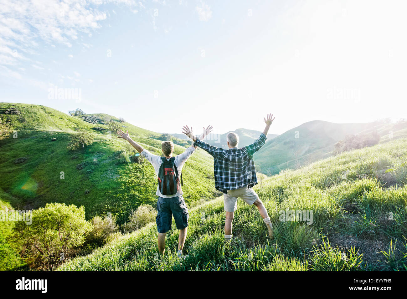 Caucasian father and son cheering on grassy hillside Stock Photo