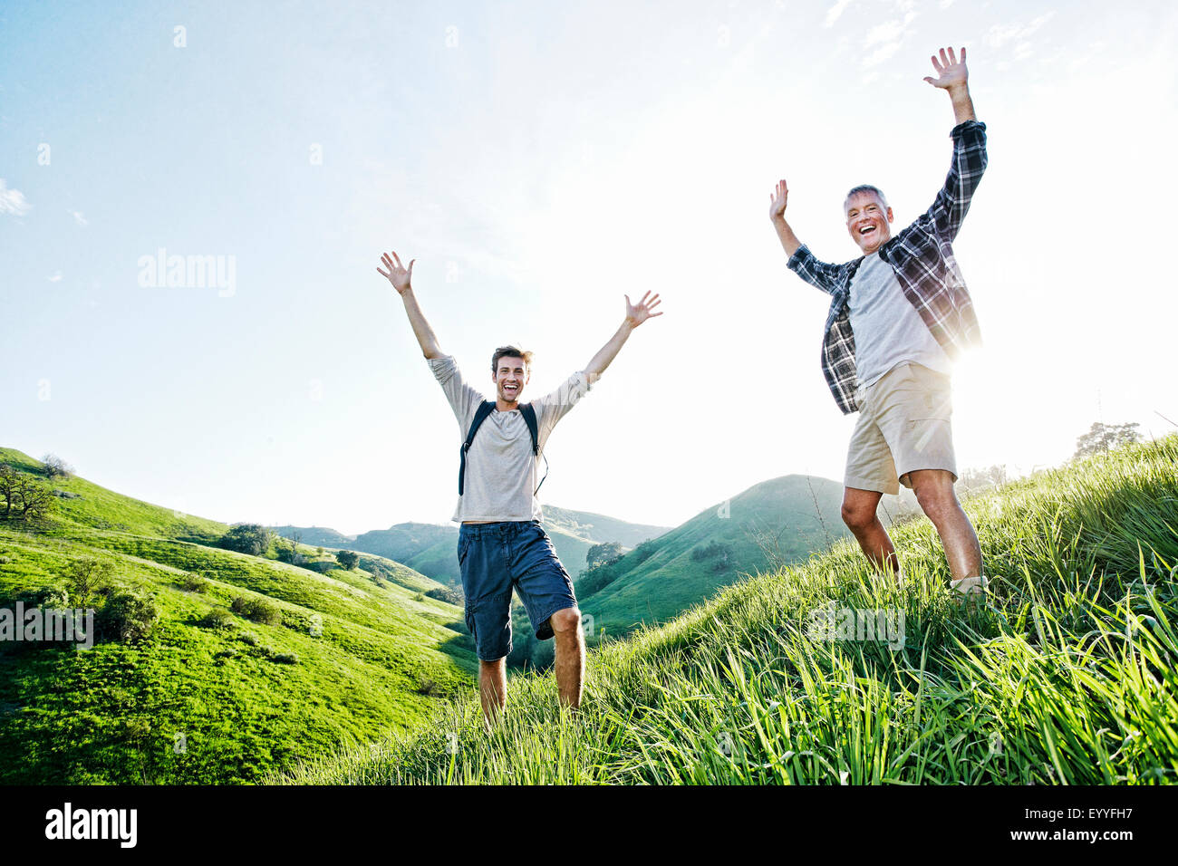 Caucasian father and son cheering on grassy hillside Stock Photo