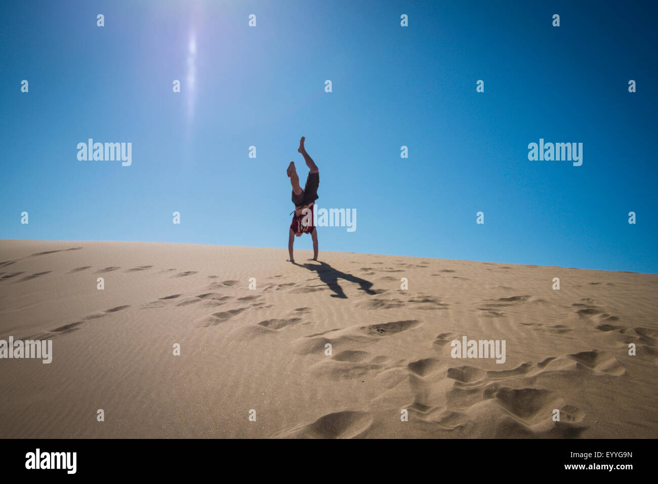 Caucasian teenage boy doing cartwheels on sand dune Stock Photo