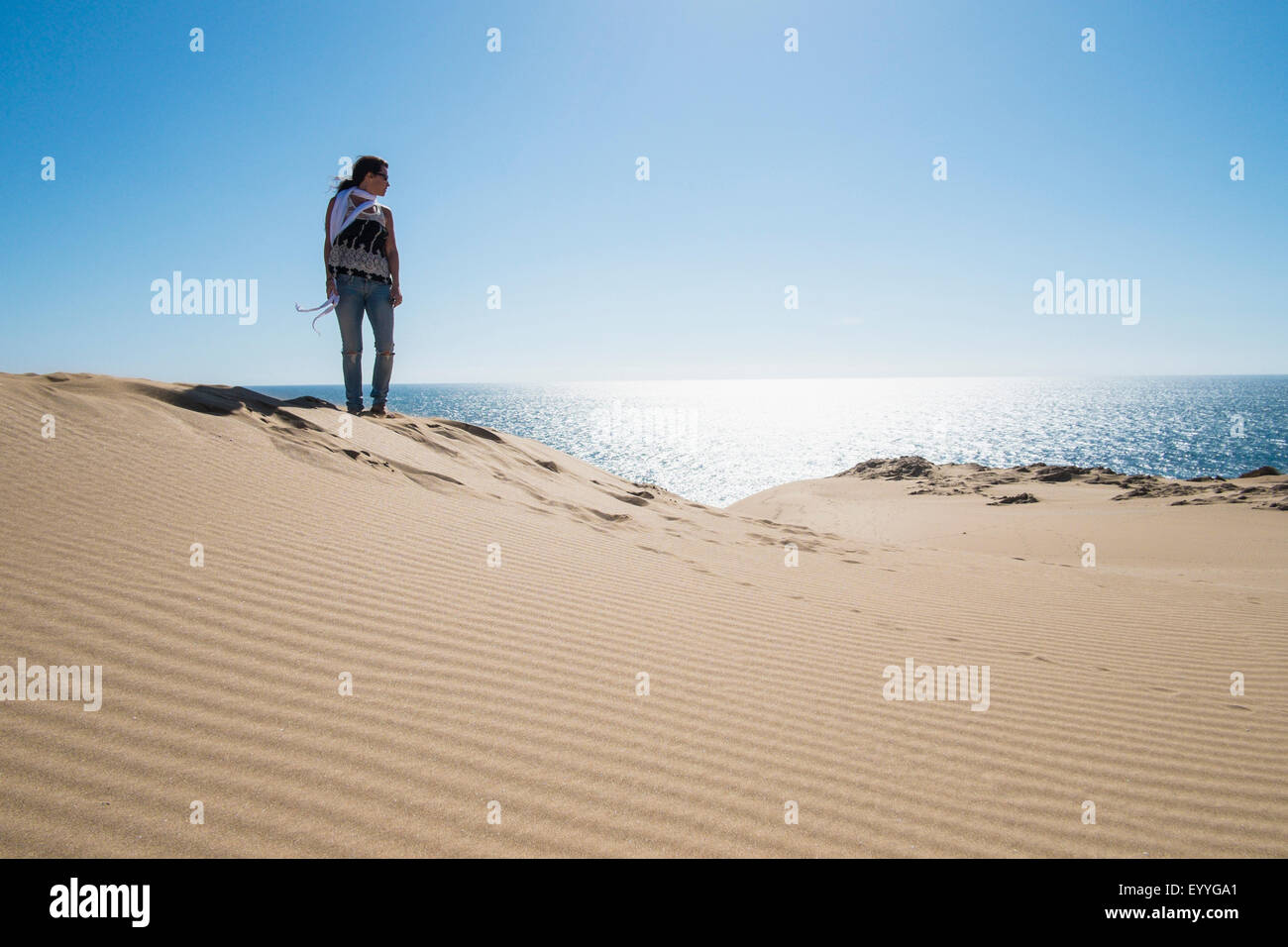 Caucasian woman standing on sand dune near ocean Stock Photo