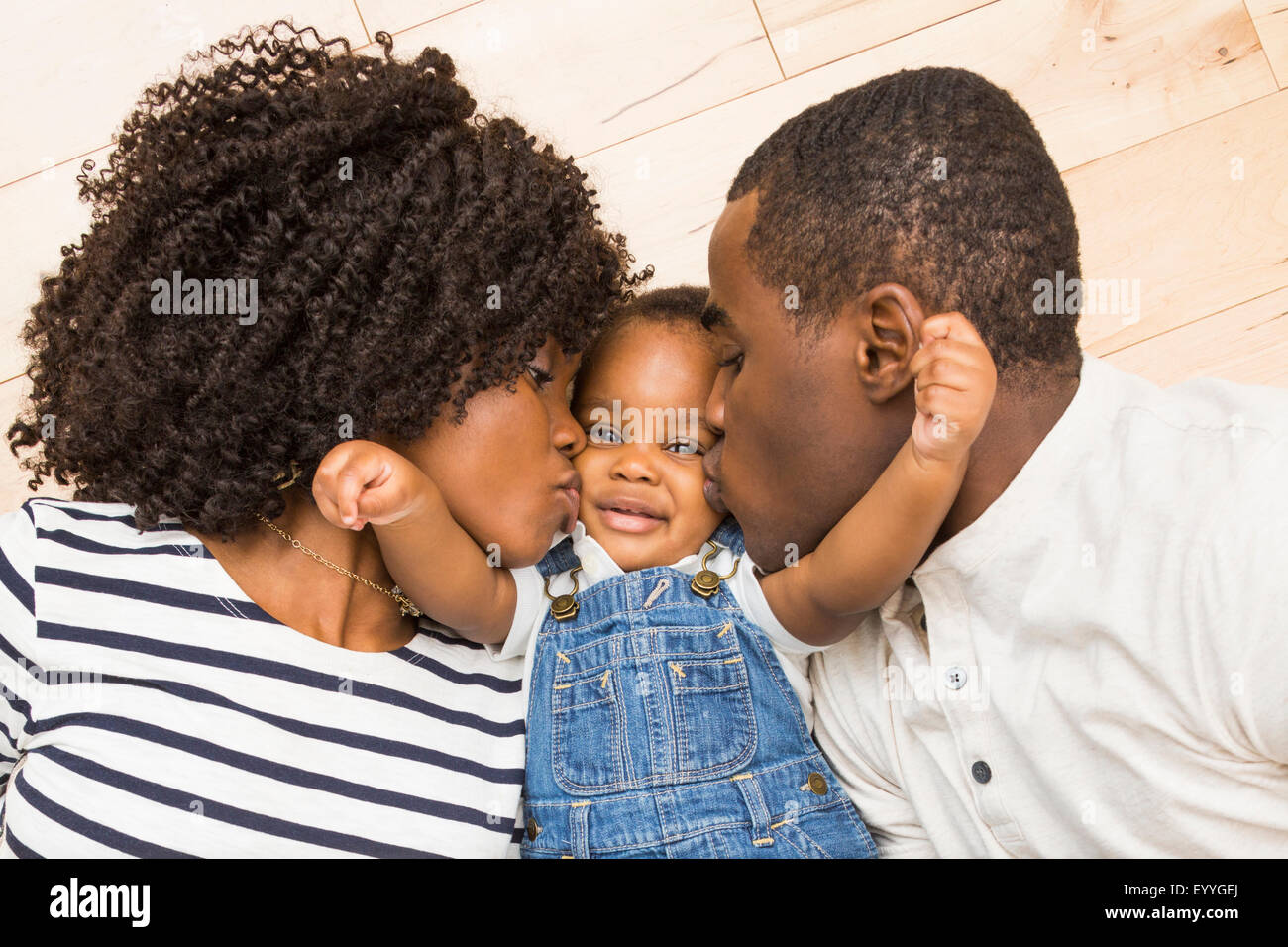 Black mother and father kissing cheeks of baby son Stock Photo
