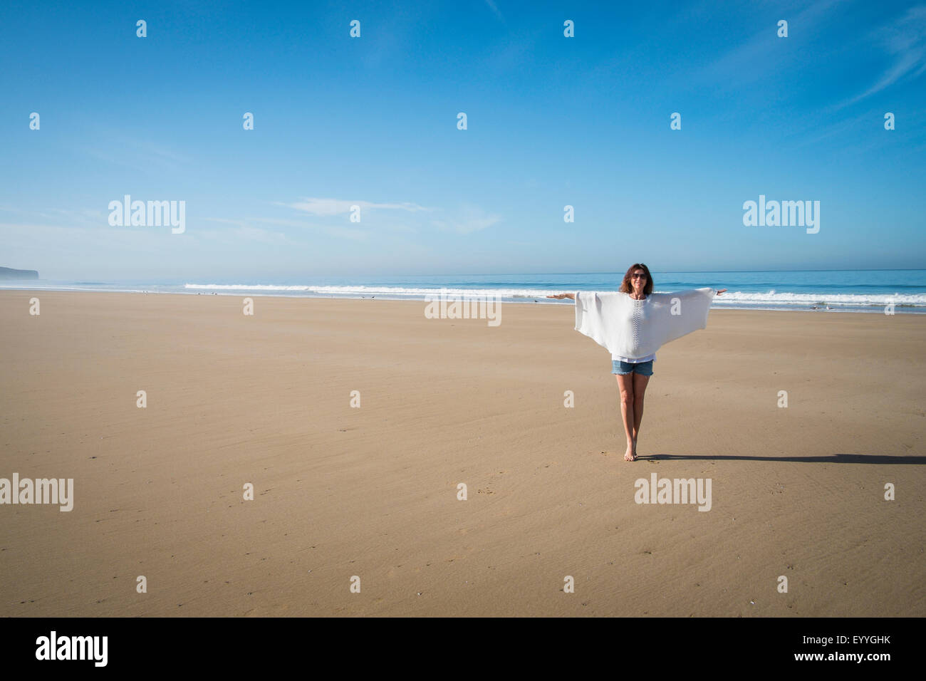 Caucasian woman walking on beach under blue sky Stock Photo