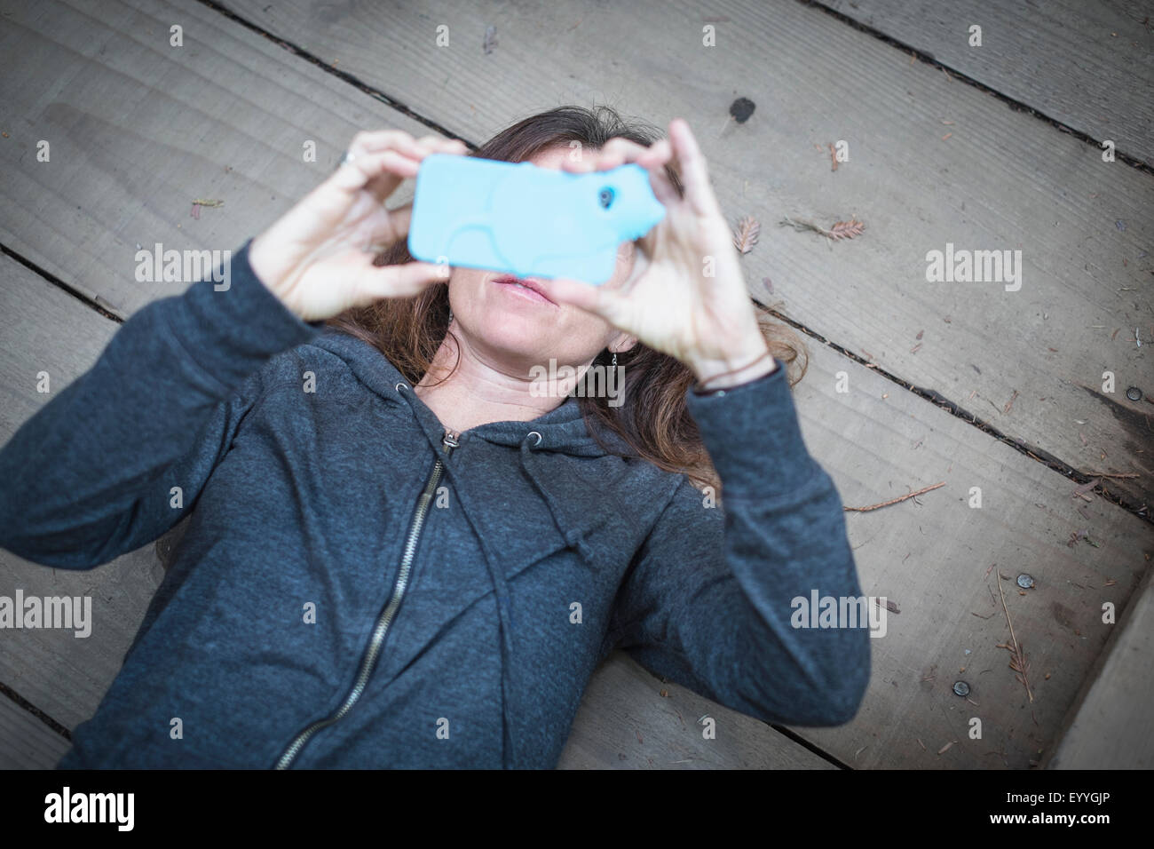 Caucasian woman laying on wooden deck taking cell phone selfie Stock Photo