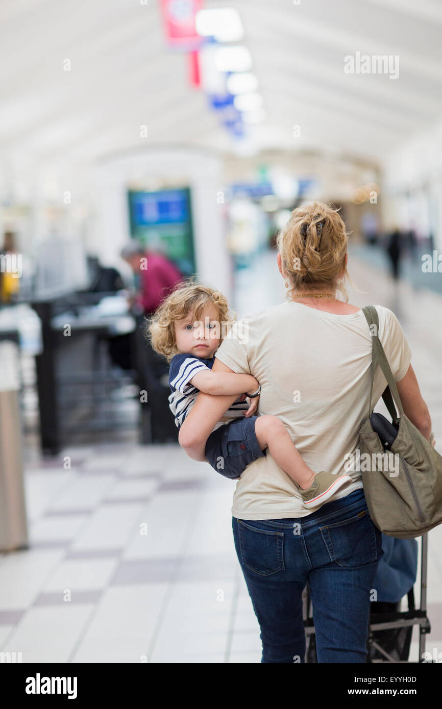 Caucasian mother carrying baby son in airport Stock Photo