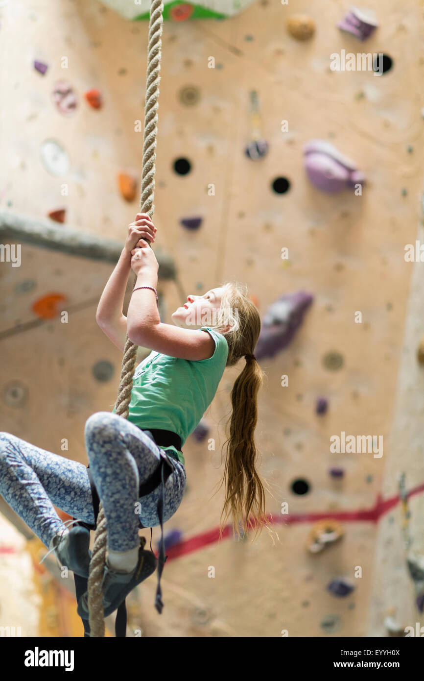 Caucasian girl climbing rope on rock wall indoors Stock Photo