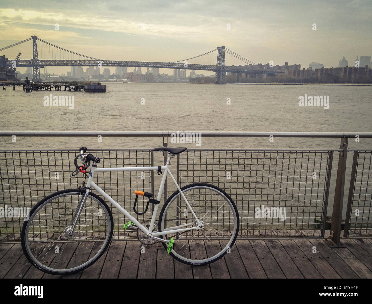 Bicycle locked to waterfront railing overlooking urban bridge, New York, New York, United States Stock Photo