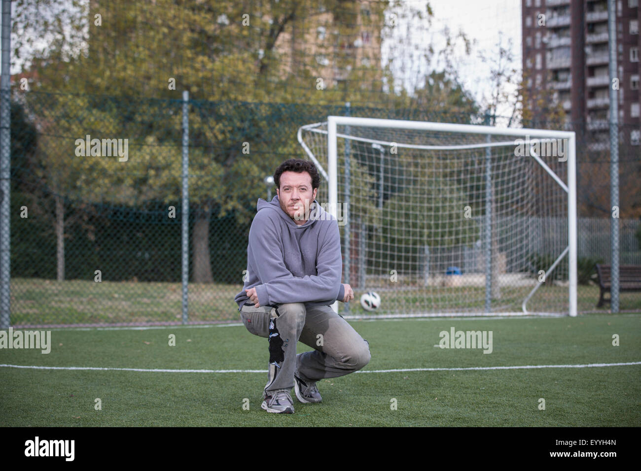 Caucasian man crouching on soccer field in urban park Stock Photo