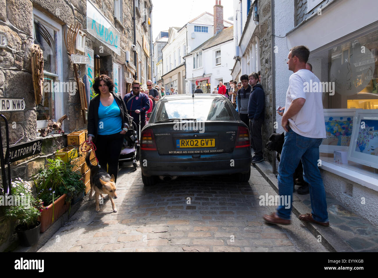 Car driving down narrow street past pedestrians in St Ives, Cornwall