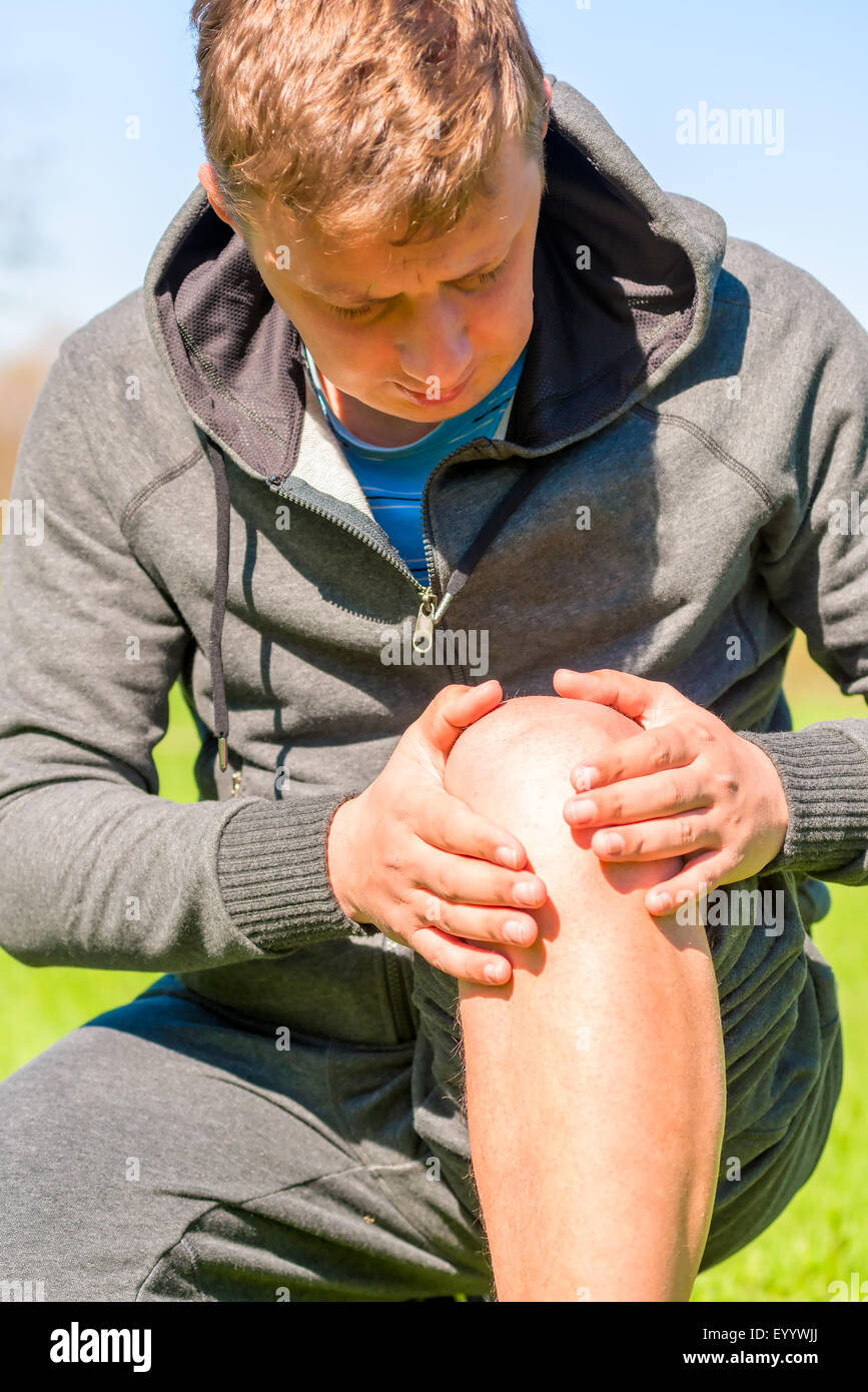 Athlete inspects diseased knee while jogging Stock Photo