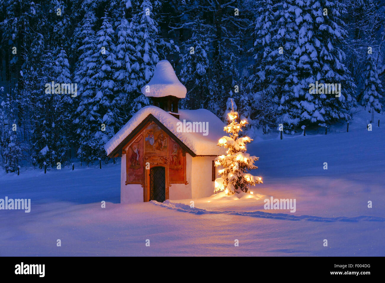 illuminated christmas tree in front of a chapel in snow landscape