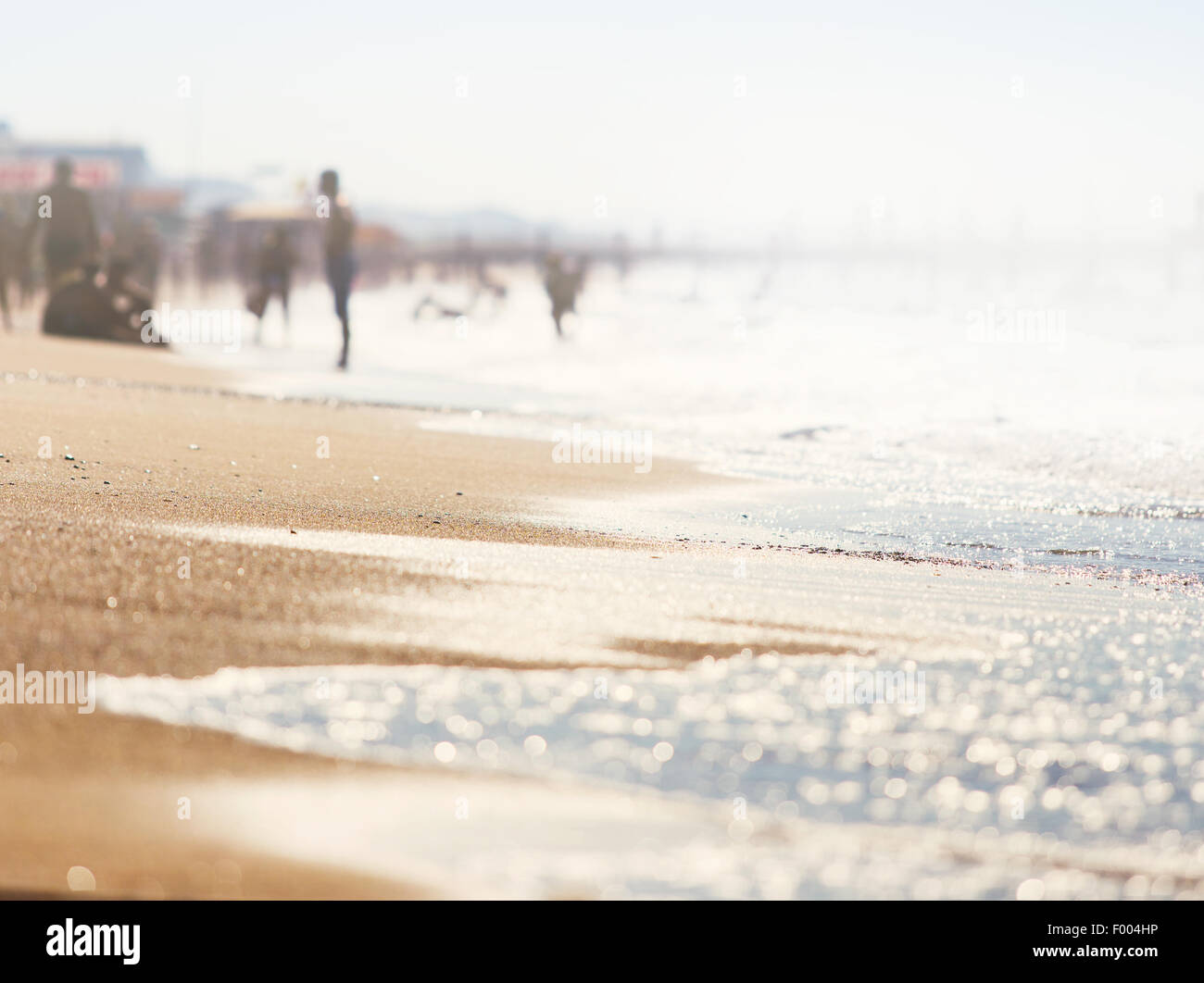 A wave thinning out of the sand of a beach, defocused people on the background Stock Photo