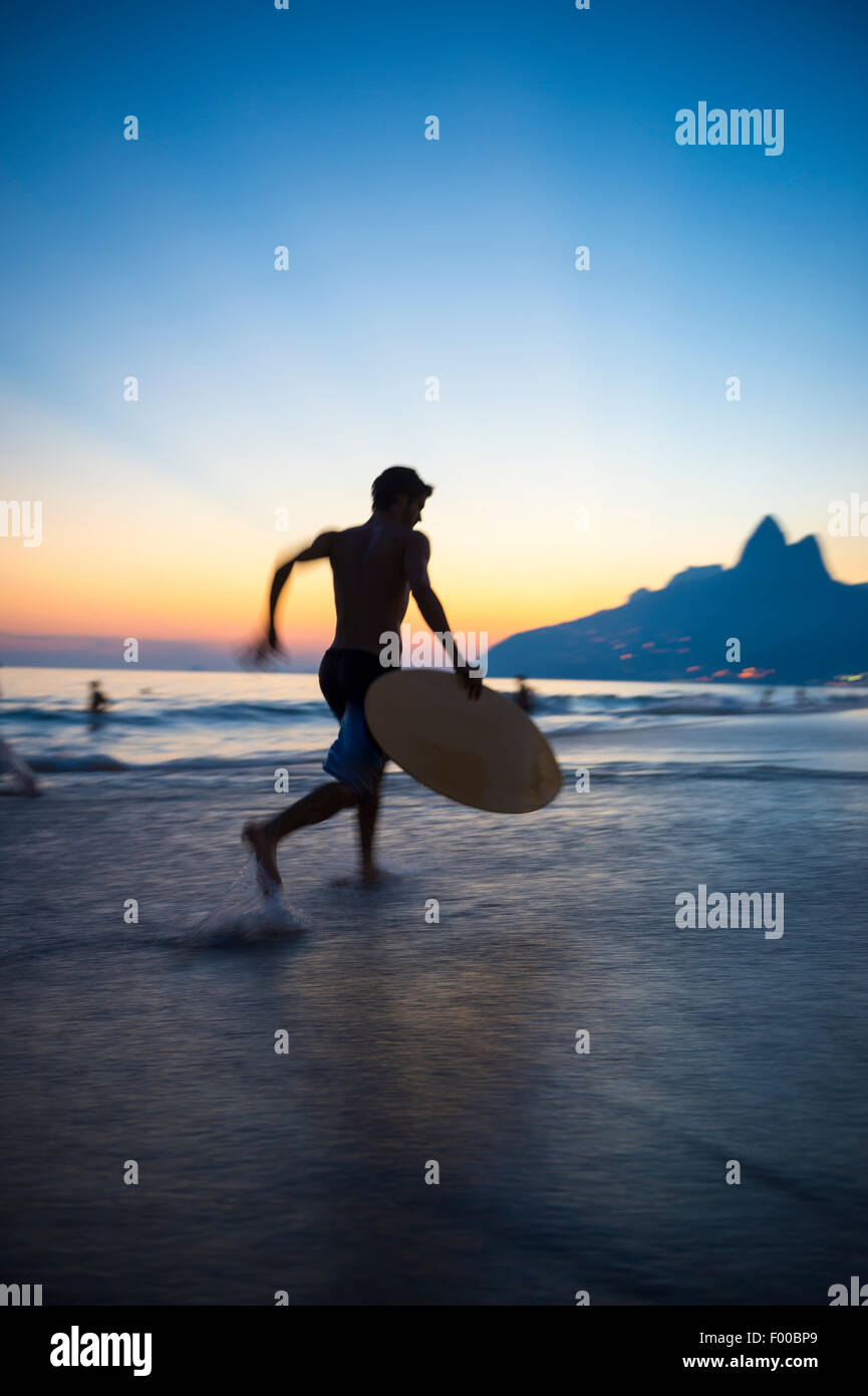 Sunset silhouette of carioca Brazilian running with skimboard on Ipanema Beach Rio de Janeiro Brazil Stock Photo