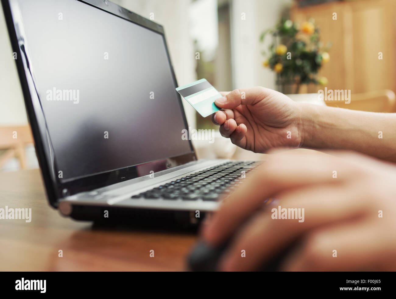 Man holding credit card in hand and entering security code using laptop keyboard Stock Photo