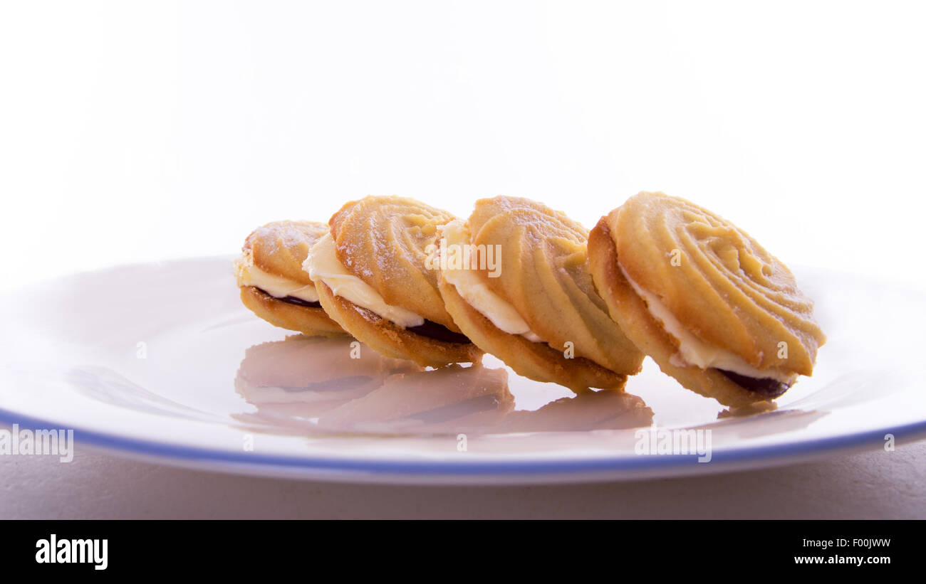 four biscuits of the same type arranged to form a line pattern and their reflection on a plate with a plain white background. Stock Photo
