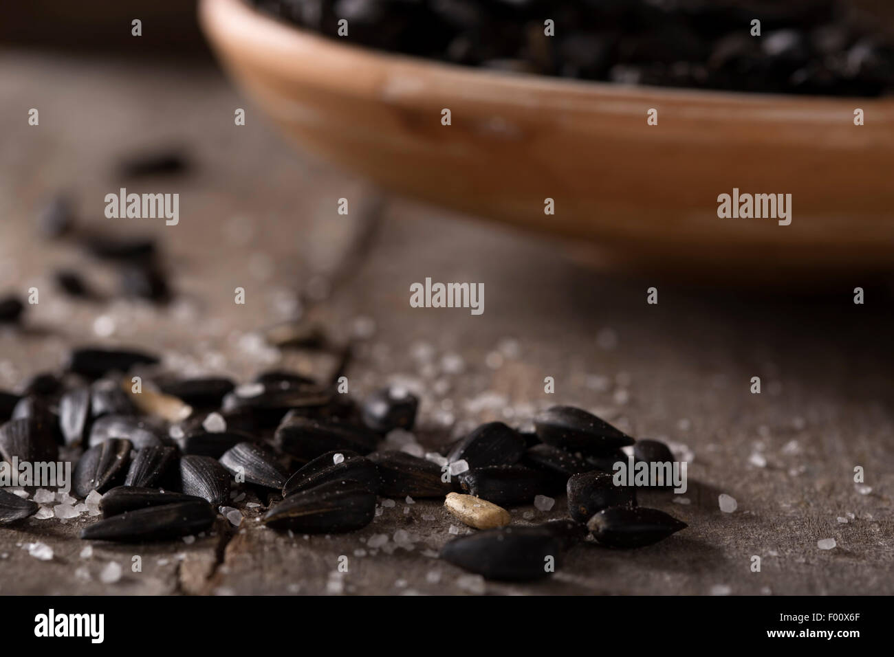 Roasted and salted sunflowers seeds in their shells, and bowl over old wood background Stock