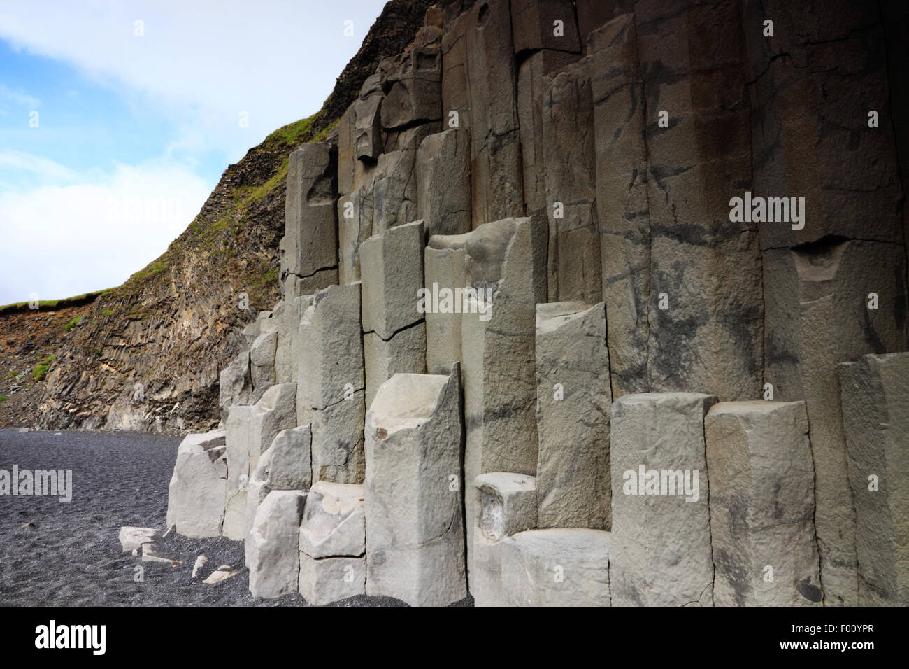 A cliff face of vertical hexagonal basalt columns with grey sand