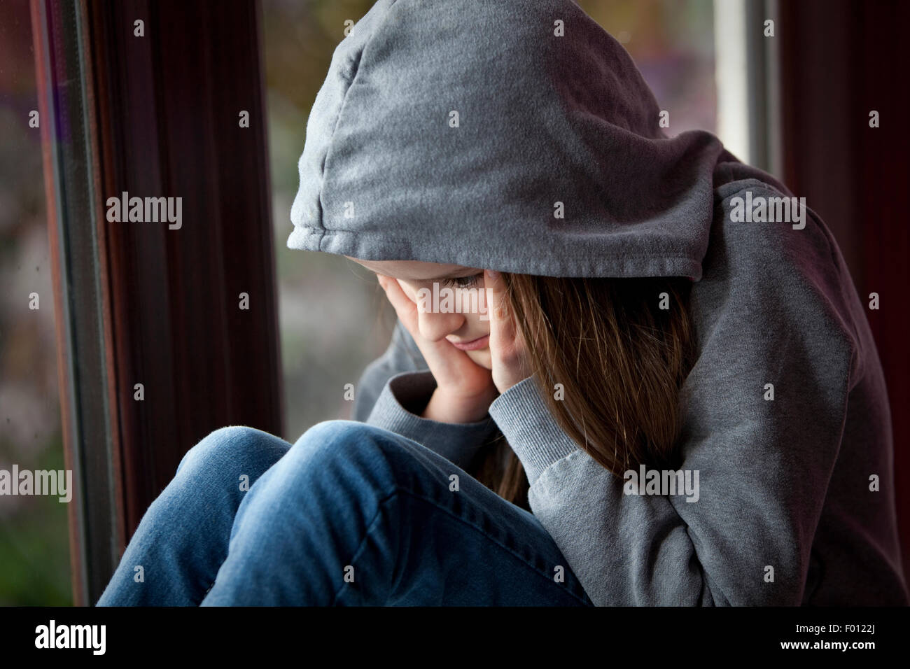 Sad girl in hooded top, sitting with face in hands in despair Stock Photo