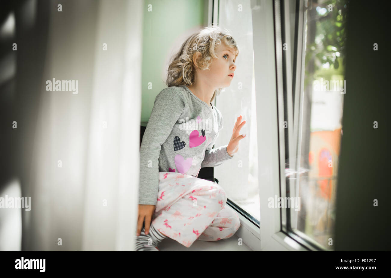 Little girl watching out of a window Stock Photo