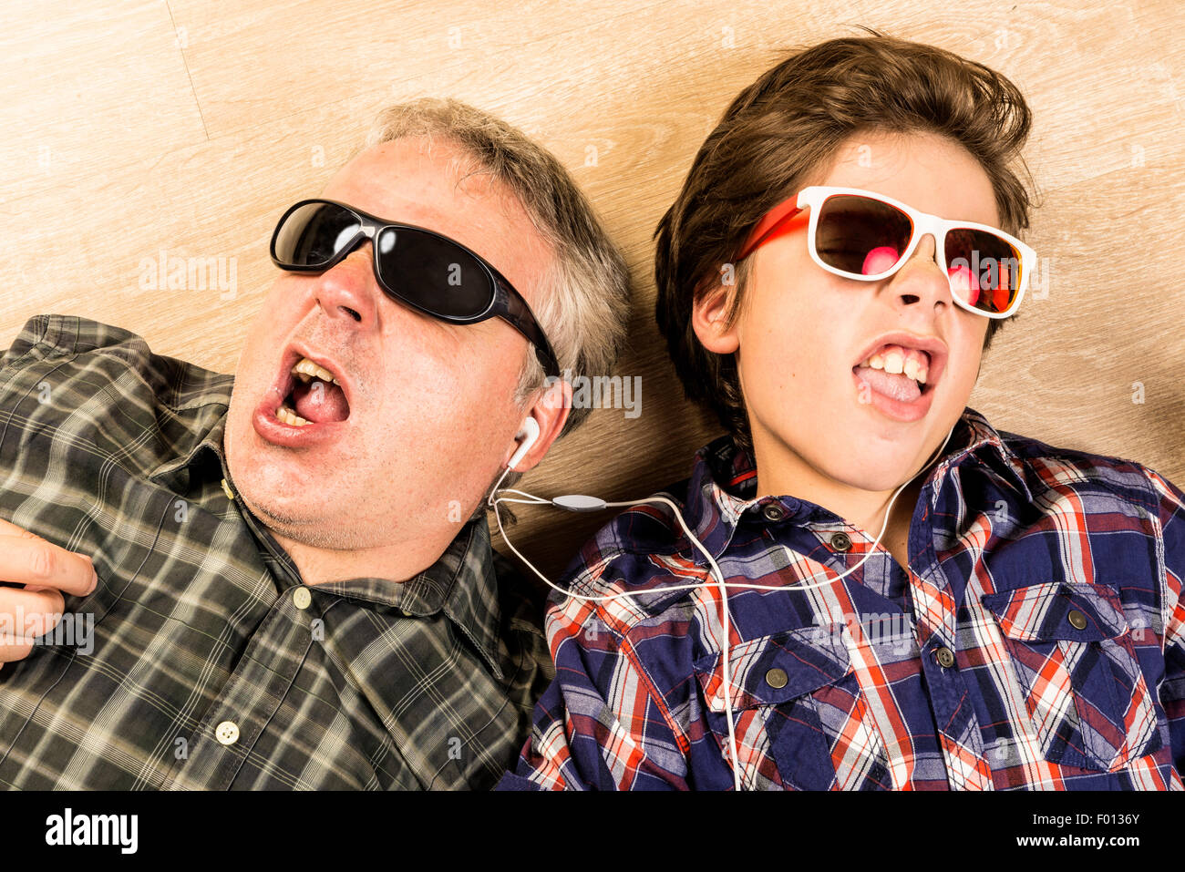 Father and son listening to music together with headphones stretched on a wooden floor at home Stock Photo