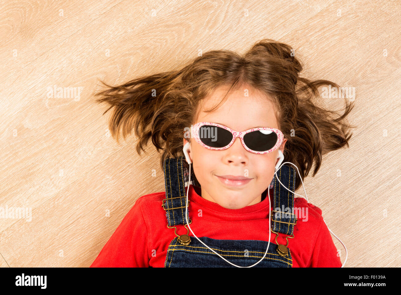 Little girl listening music with headphones and sunglasses stretched on