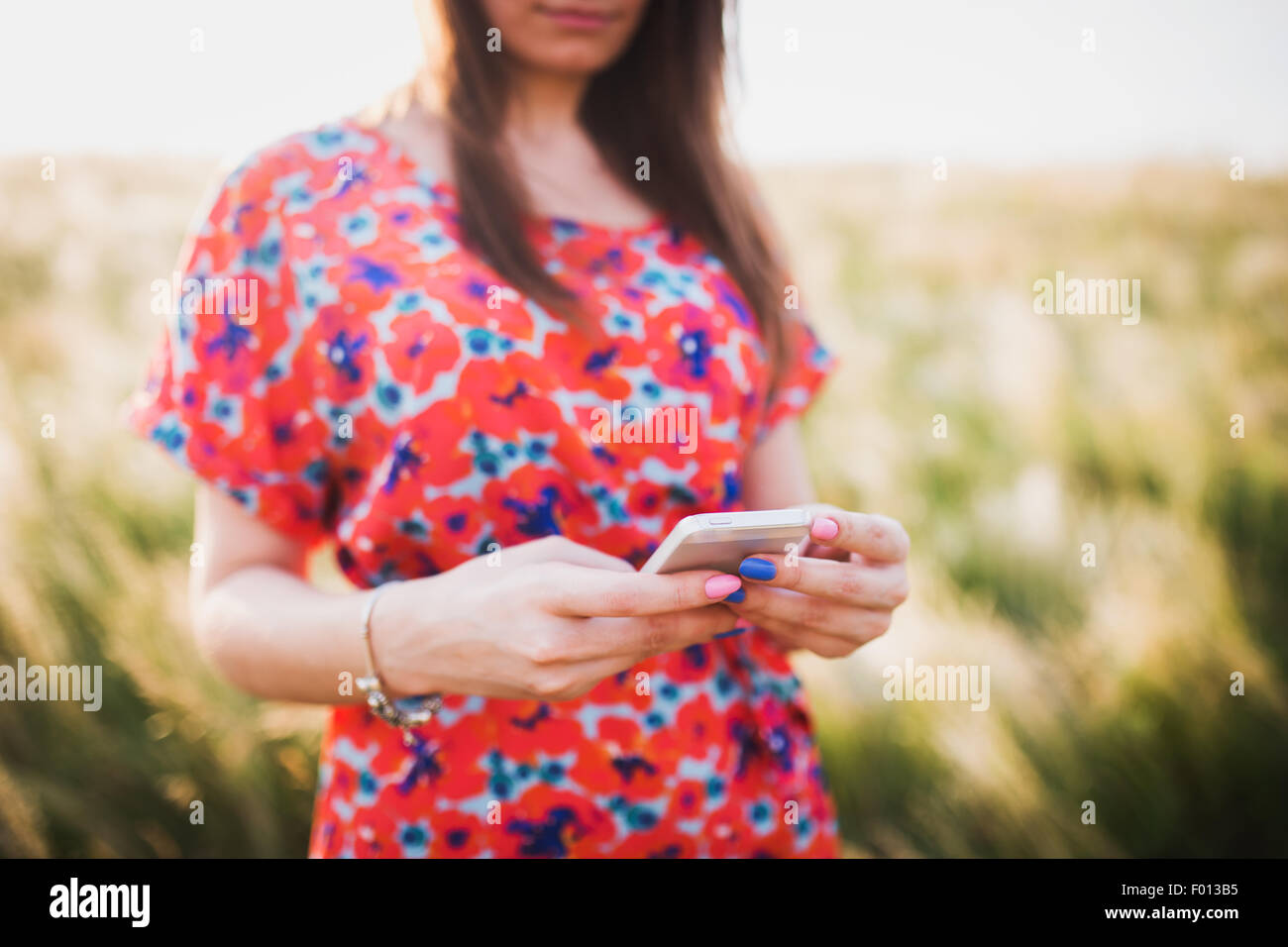 Charming young woman using to mobile smart phone, against green of summer Stock Photo