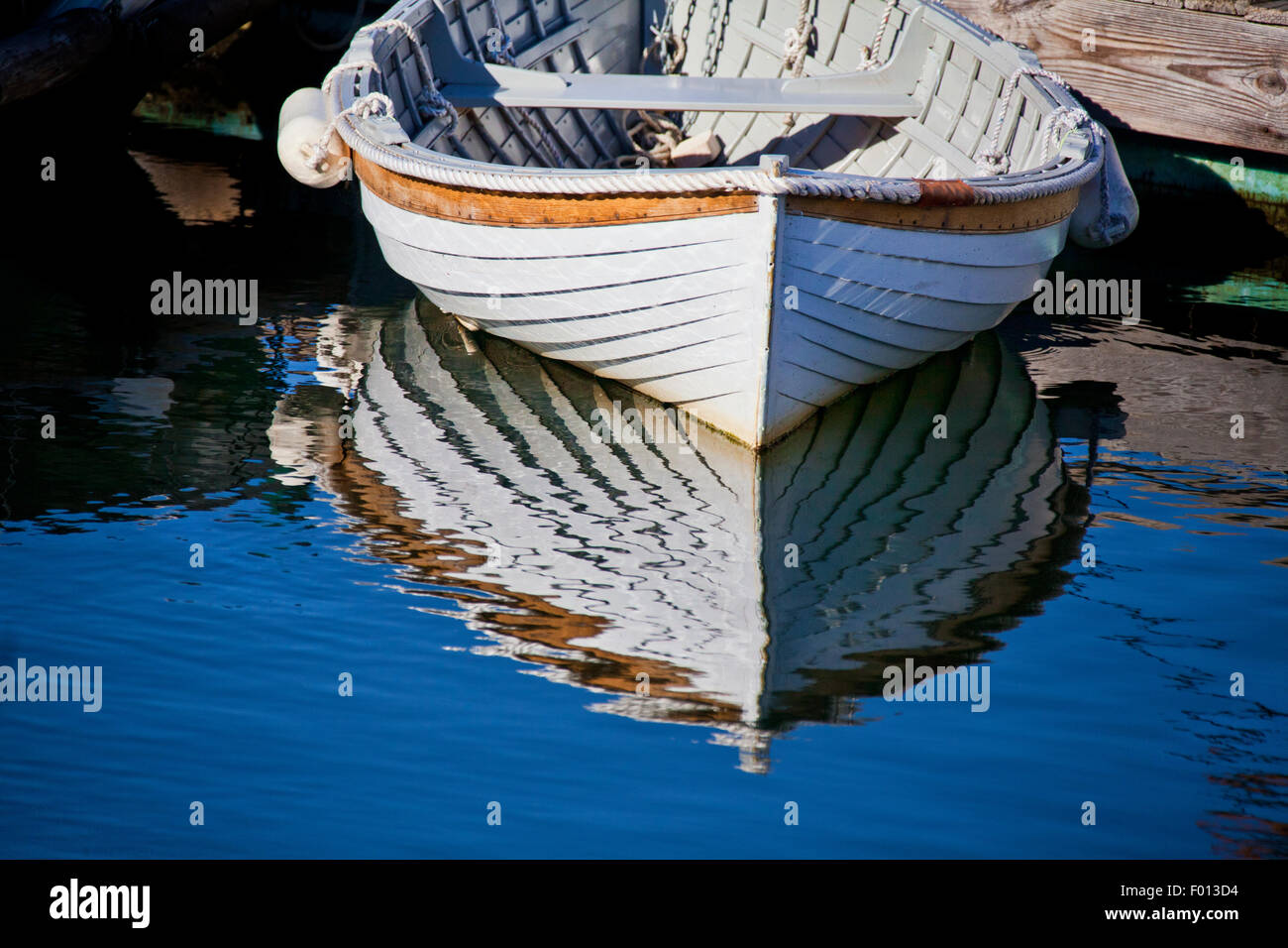 Pleasing reflections of a bright white wooden dinghy tied to a wooden dock in Camden Harbor in Maine Stock Photo