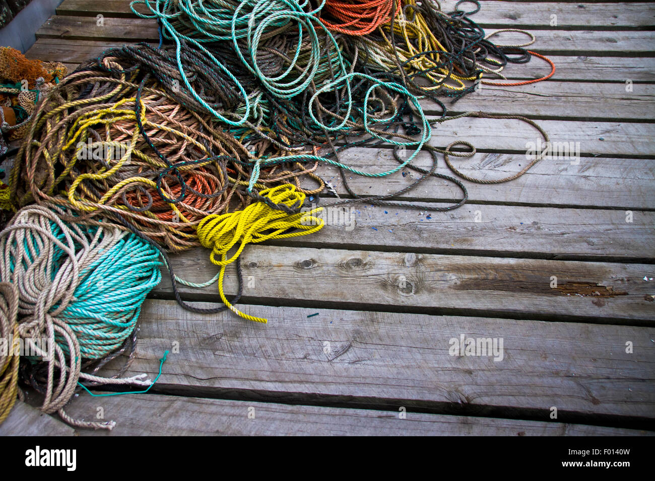 A mess of dock lines tangled with various nautical ropes sitting on a wooden dock along the Maine Coastline Stock Photo