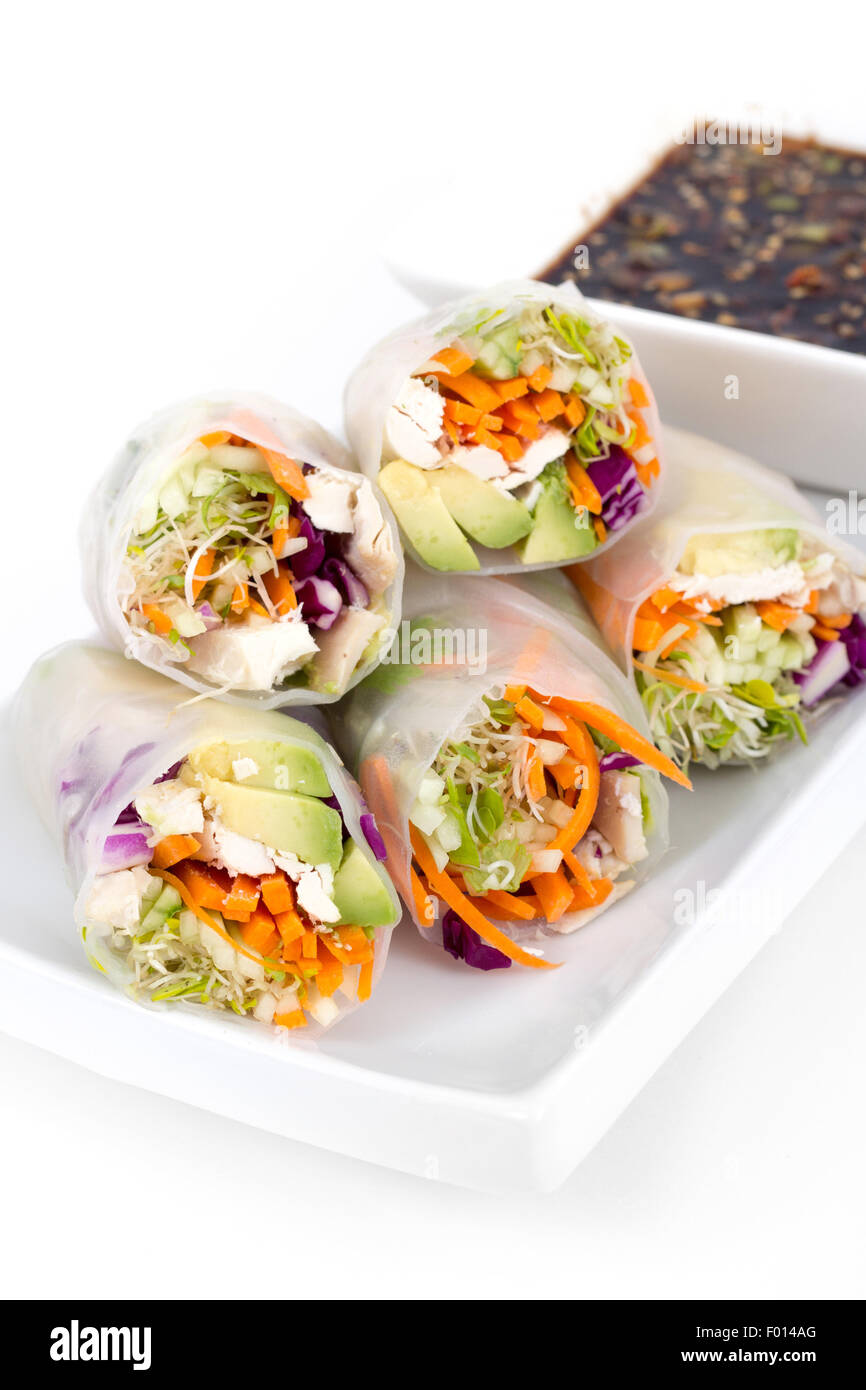 colourful chicken, sprouts and avocado rice paper spring rolls with soy base dip sauce over white background Stock Photo