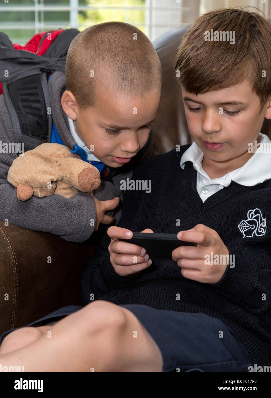 Younger Brother (Age 7) Watching Older Brother (Age 9) Using his iPod.  MR Stock Photo