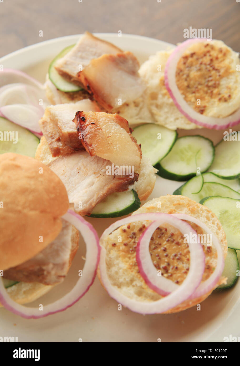 Sliced roast pork belly with cucumber and onion slices on rolls spread