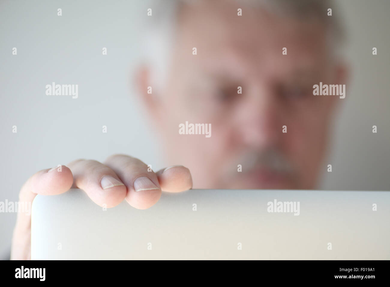 Older man has hand on his laptop, face defocused Stock Photo