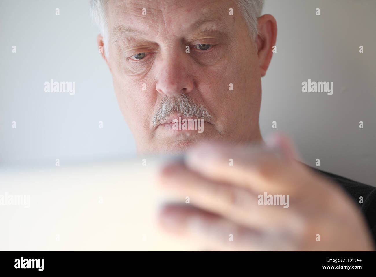 A senior man with a hand on his laptop cover checks his screen. Stock Photo