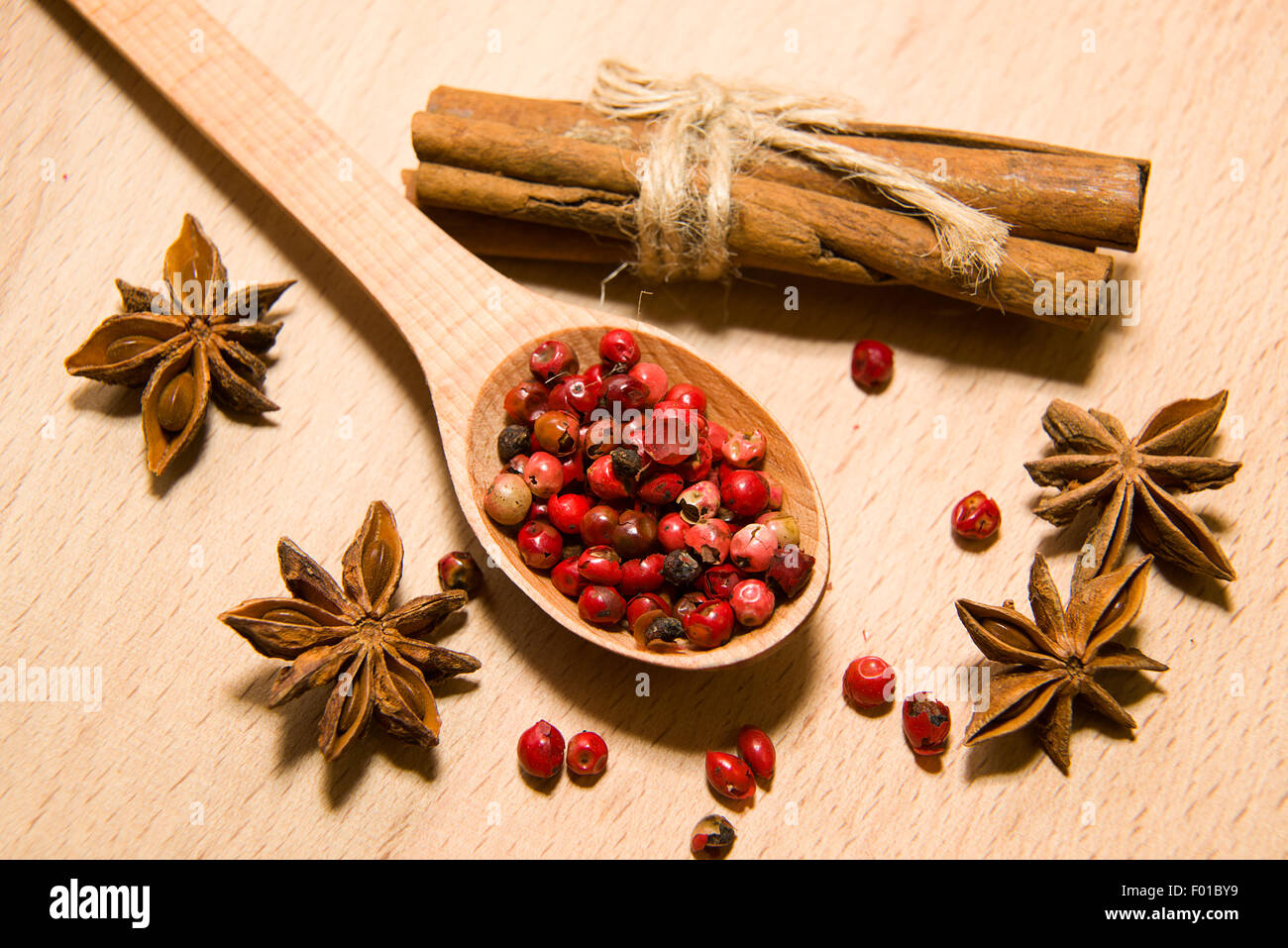 wooden Spoon with a mixture of grains of pepper, cinnamon and star anise on a wooden surface Stock Photo