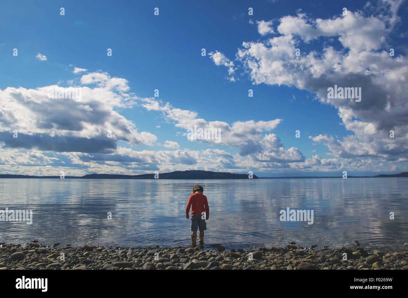 Rear view of boy standing at the water's edge Stock Photo