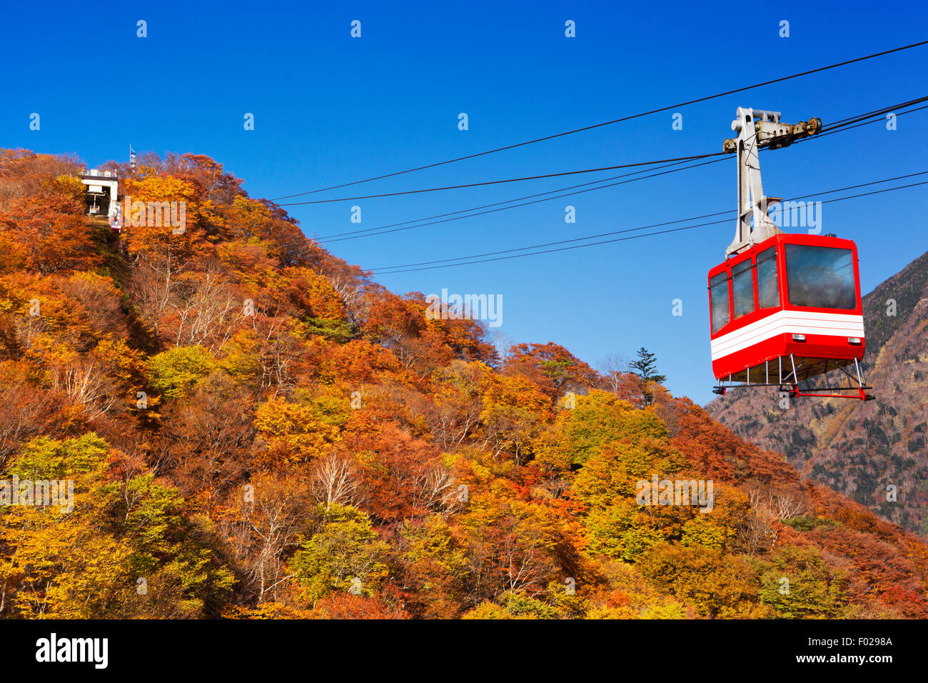 A cable car moving up a mountain covered in bright autumn colours. Photographed at the Akechidaira Ropeway near Nikko, Japan. Stock Photo