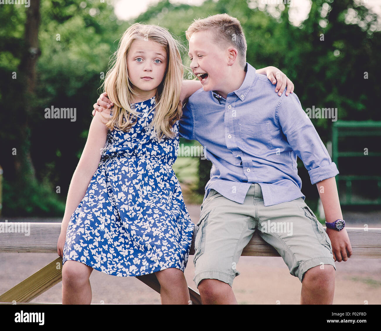 Boy and girl sitting on wooden gate with their arms around each other Stock Photo