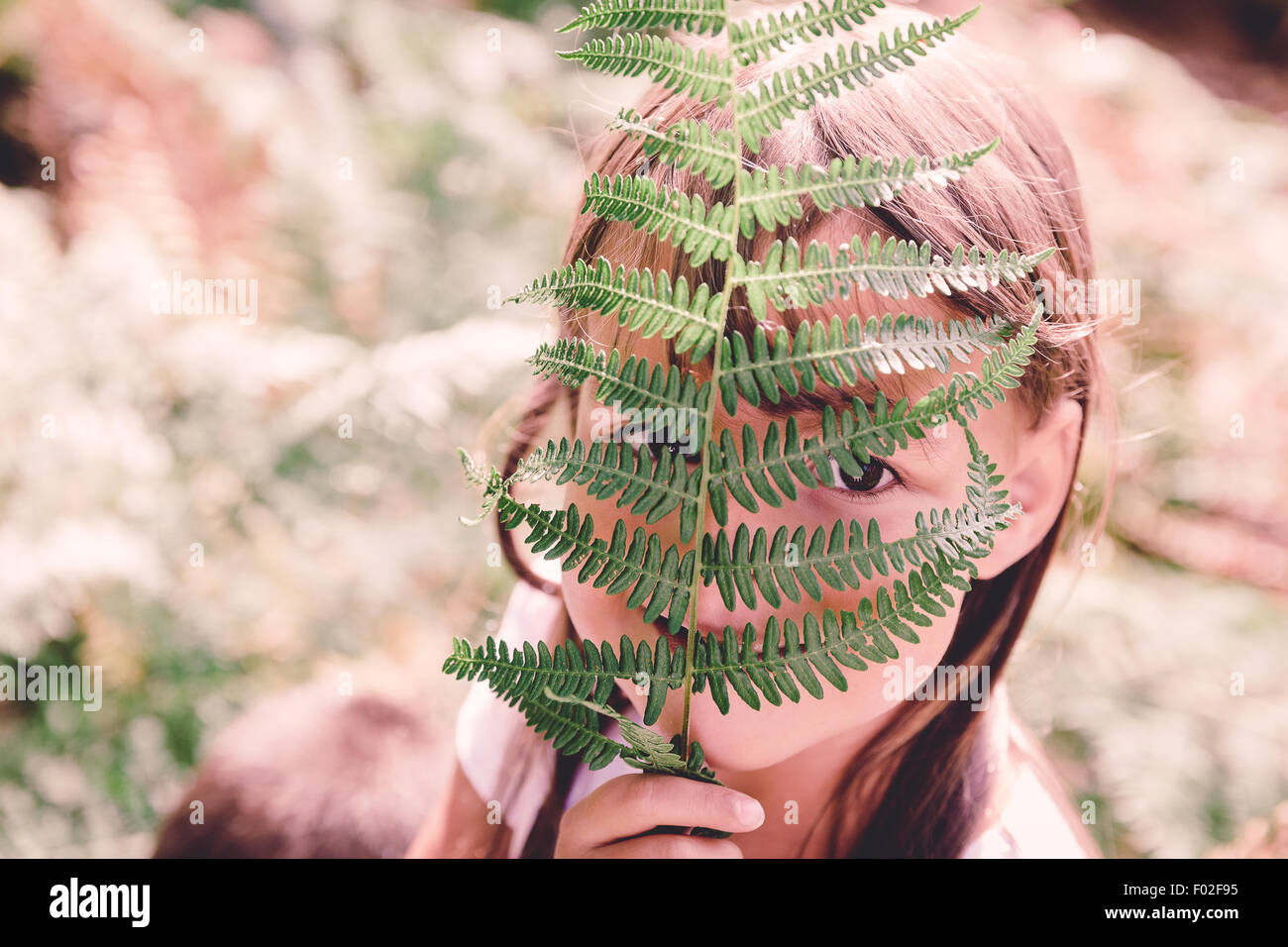 Girl hiding her face behind a fern frond Stock Photo