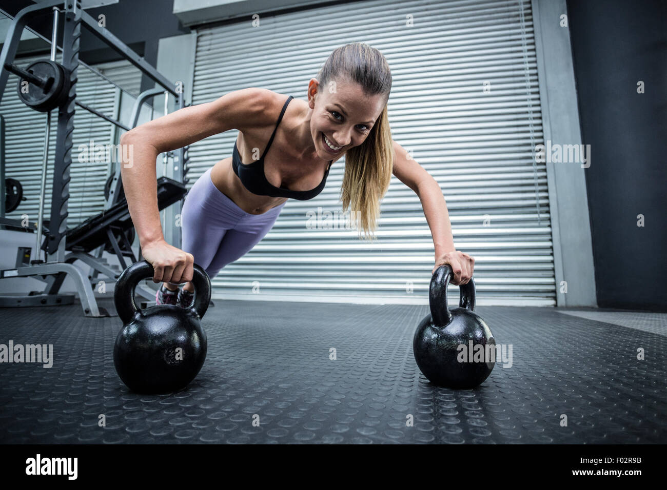 Muscular woman doing pushups with kettlebells Stock Photo
