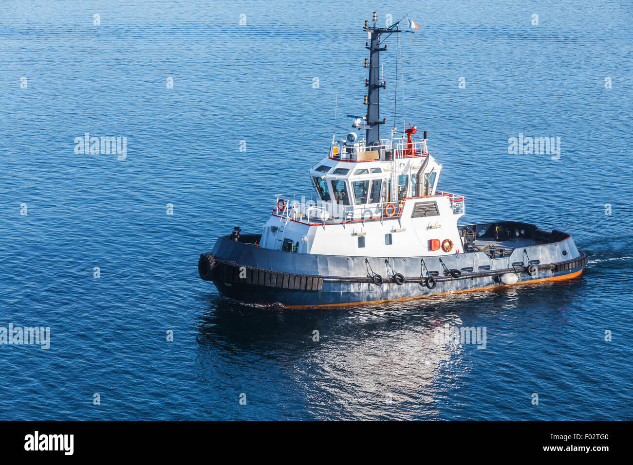 Small tug boat with white superstructure and dark blue hull underway on sea water Stock Photo