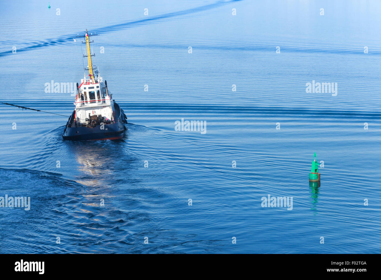 Small tug boat with white superstructure and dark blue hull goes on a fairway Stock Photo