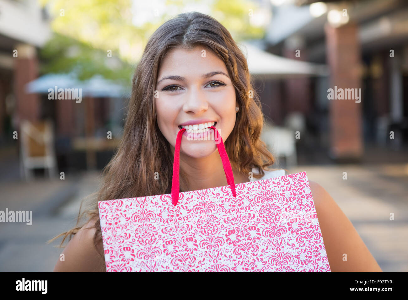 Portrait of smiling woman holding shopping bag in her mouth Stock Photo