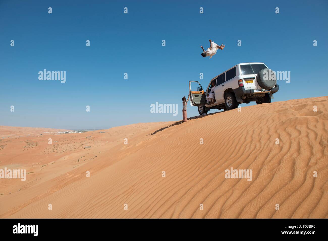 Omani youth jumping from a vehicle in desert sand dunes. Stock Photo