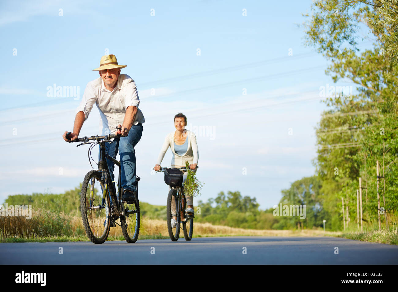 Senior couple riding bikes through summer landscape on a road Stock Photo
