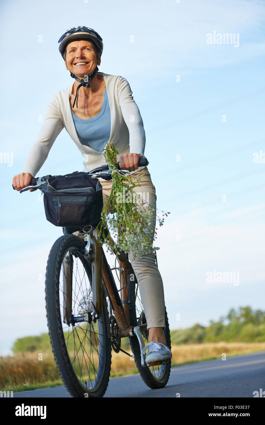 Smiling woman riding bike with helmets on a road in summer Stock Photo