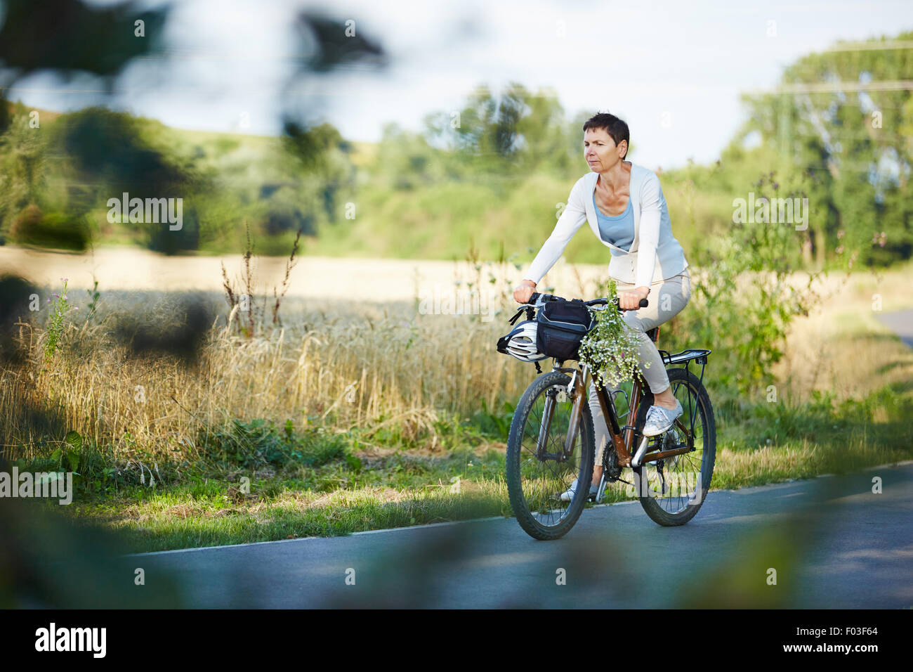 Old woman riding her bike on a street in summer Stock Photo
