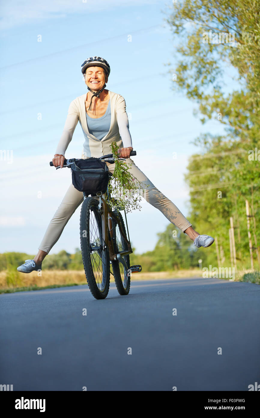 Smiling old woman stretching her legs while cycling in summer Stock Photo