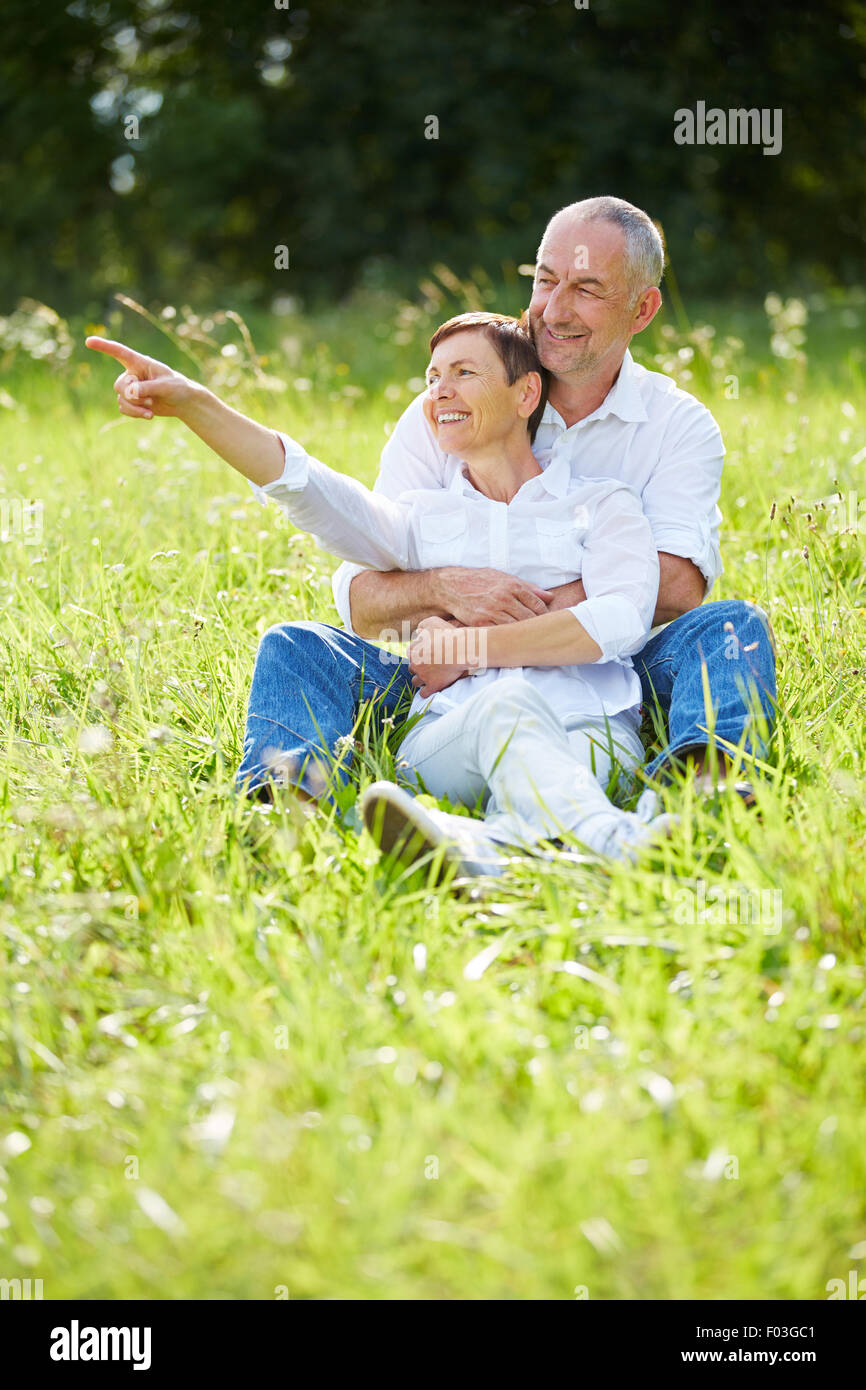 Senior couple sitting in grass in nature and woman pointing into the distance Stock Photo