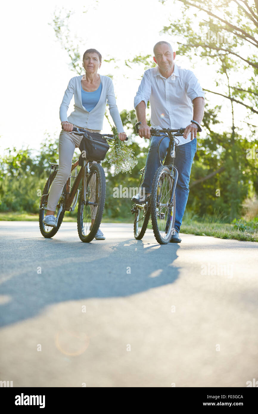Happy senior couple riding bike in summer in nature Stock Photo