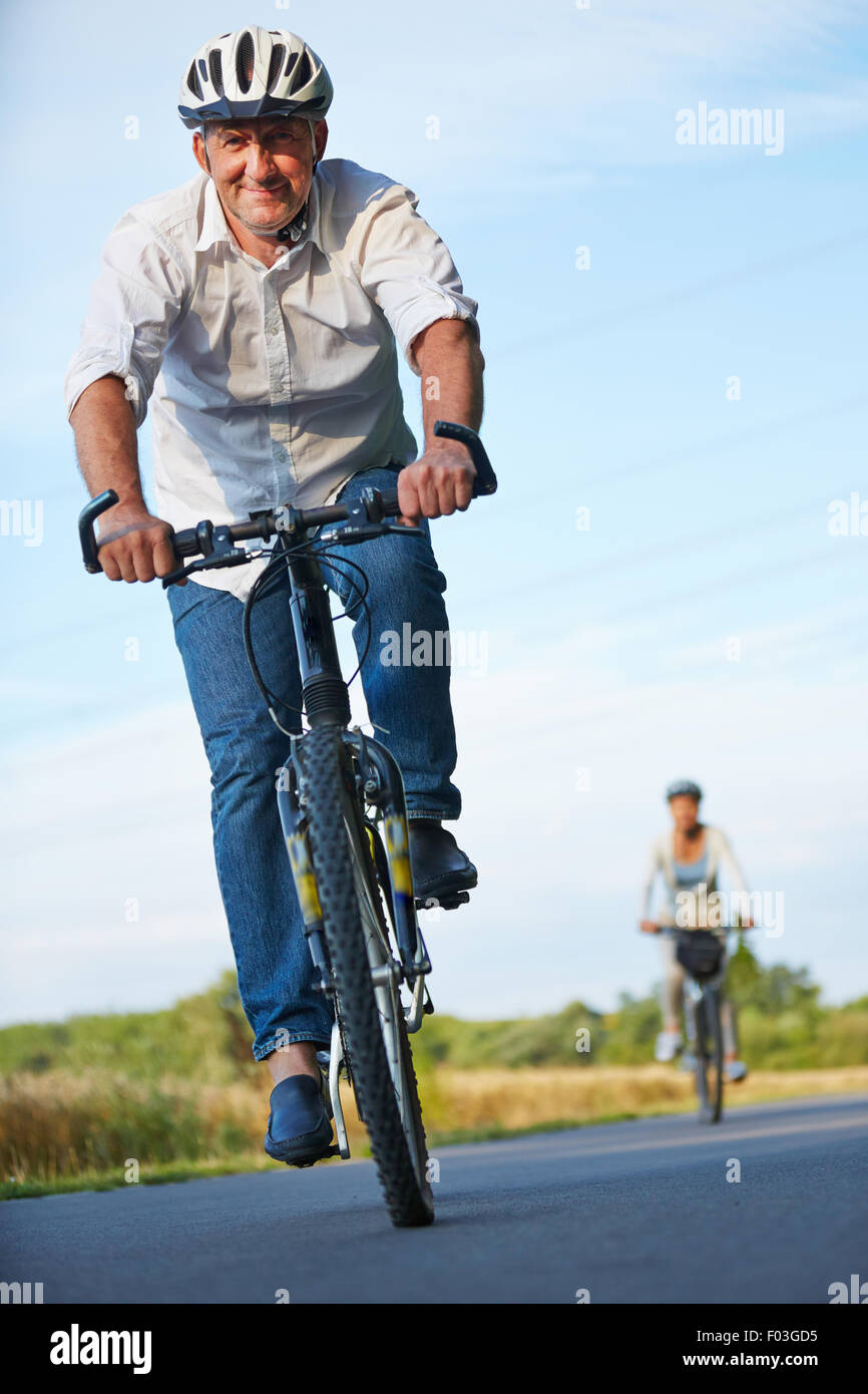Senior people with bike helmets cycling in summer Stock Photo